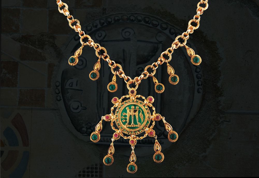 Collier in oro realizzato interamente a mano in stile Magno - Greco. Nella parte centrale è stato creato lo Statere (antica moneta di Kroton - 510-490 a.C) sovrapposta su una base di pasta vitrea. Nel collier sono stati incastonati rubini e smeraldi di taglio cabochon.